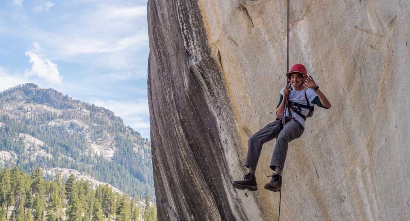 A person wearing safety gear is secured by ropes mid-air against a rock wall.